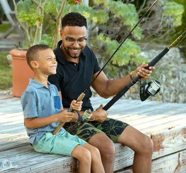 Father and son fishing together, sitting on a dock, bonding and enjoying nature in a peaceful setting.