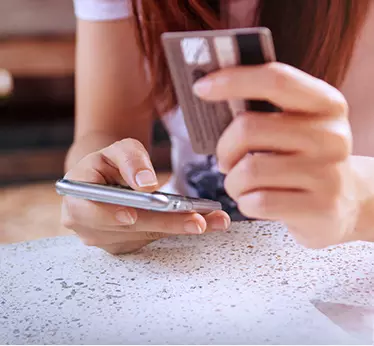 Close-up of a woman's hand holding a smartphone and credit card, symbolizing online shopping or mobile banking convenience.